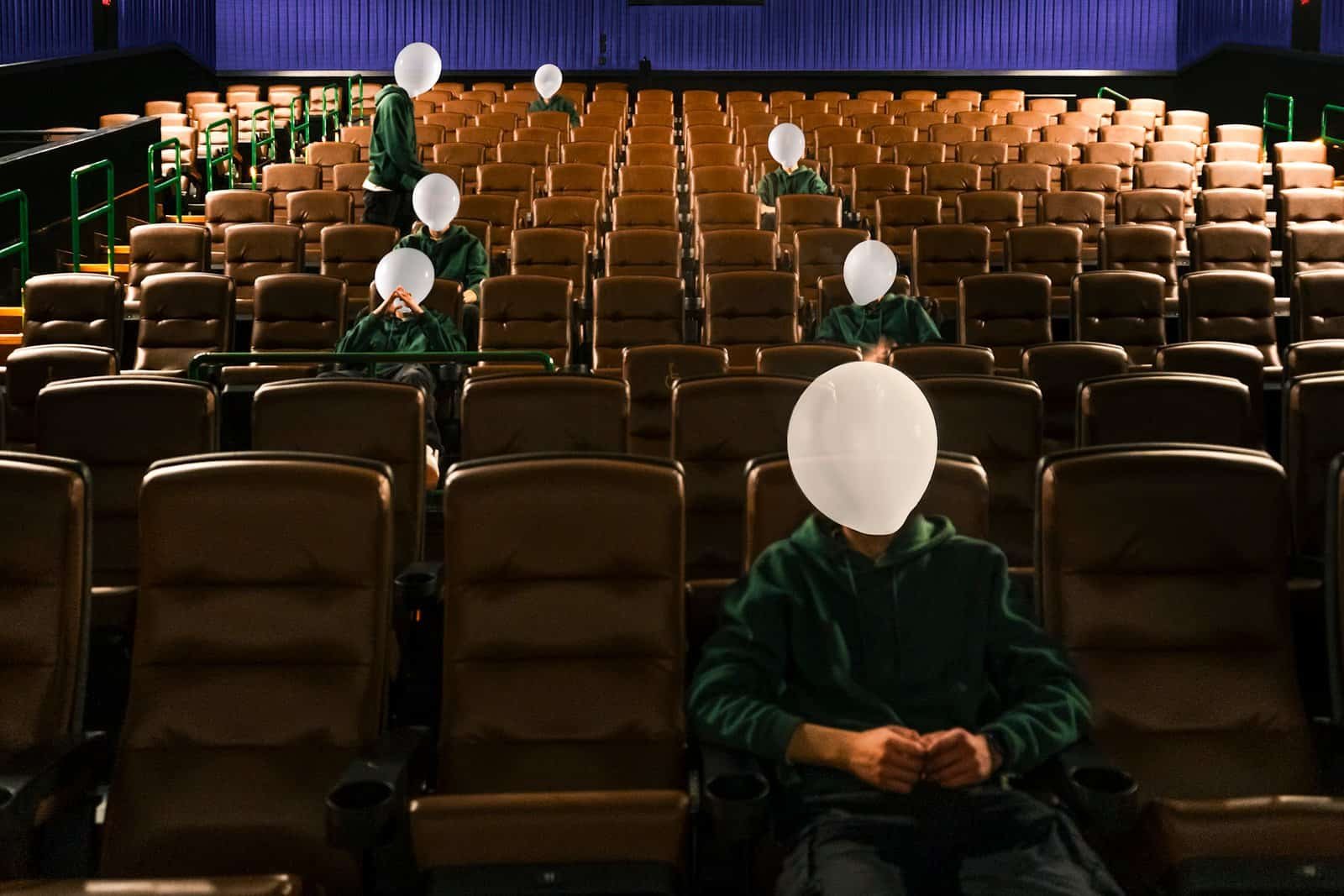 Group of faceless people with balloons sitting in a theater.
